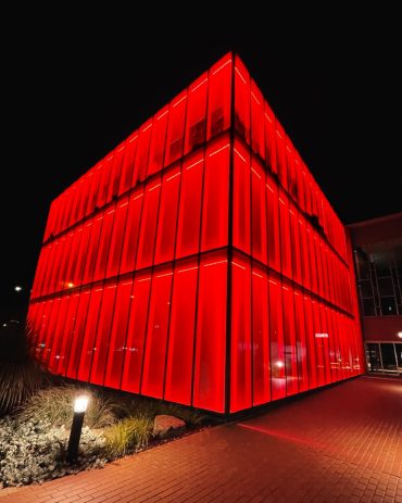 The glass cube building of broadmeadows town hall is seen from the pathway illuminated in red